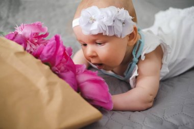 Yatakta yatıyordu ve ping buket pion çiçek ile oynayan sevimli bebek