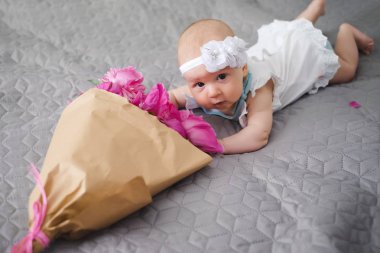 Yatakta yatıyordu ve ping buket pion çiçek ile oynarken mutlu yeni doğan bebek