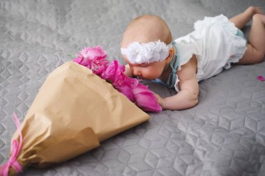 Yatakta yatıyordu ve ping buket pion çiçek ile oynayan sevimli bebek