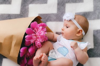 Yatakta yatıyordu ve ping buket pion çiçek ile oynamaya yeni doğan bebek