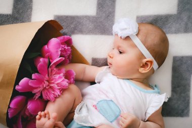 Yatakta yatıyordu ve ping buket pion çiçek ile oynayan sevimli bebek