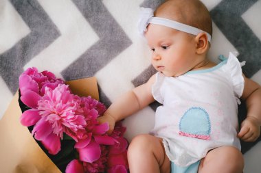 Yatakta yatıyordu ve ping buket pion çiçek ile oynamaya yeni doğan bebek