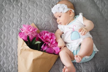 Yatakta yatıyordu ve ping buket pion çiçek ile oynarken mutlu yeni doğan bebek