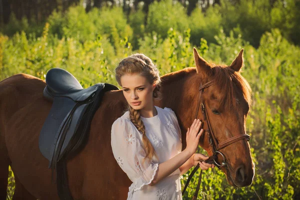 Woman standing with horse near forest and touching to horse face