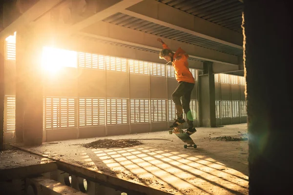 Extreme street sport. Hipster man jumping and riding on long board at an abandoned building at sunset. Image with grain