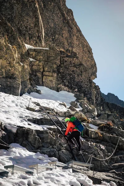 Female hiker climbing up on ladder to the mountain top in winter. Rysy. Slovakia.