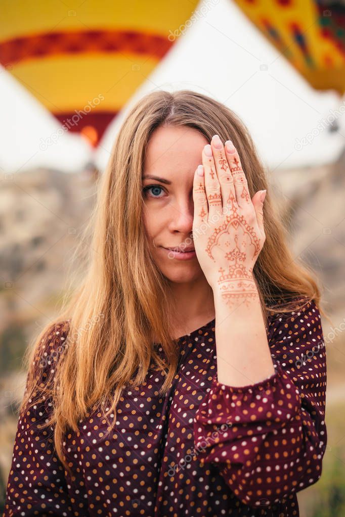 Closeup woman portrait with beautiful eyes and mehendi henna tattoo on hand in Cappadocia landscape and hot air balloon on background at sunset