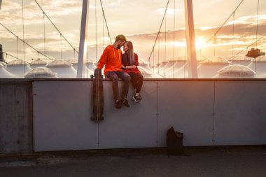 Elele ve çatıda oturan ve gün batımı vaktinizi gülümseyen güzel genç çift