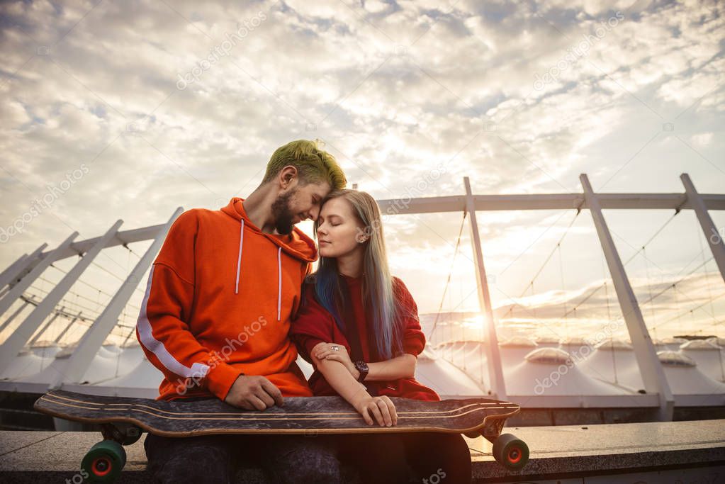 Beautiful young couple holding hands and smiling while sitting on the roof and enjoying sunset time