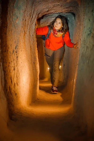 Beautiful tourist woman explore long narrow tunnel in ancient Derinkuyu underground cave city. Travel to Turkey