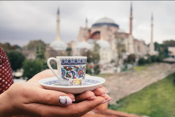 Cup of turkey coffee in tourist woman hands on Hagia Sophia famous islamic Landmark mosque, Travel to Istanbul, Turkey background