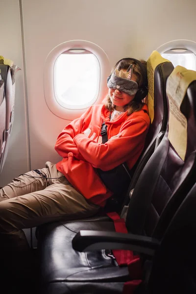 Tourist woman passenger fly in airplane and sleep in eyes mask near the window