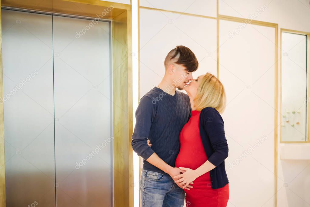 Beautiful pregnant woman with husband waiting elevator and for coming back to home