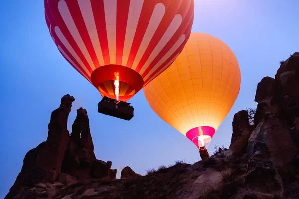 Colorful hot air balloons flying over beautiful Goreme landscape at night on blue sky before sunrise. Cappadocia mountains, Turkey. High ISO image with grain