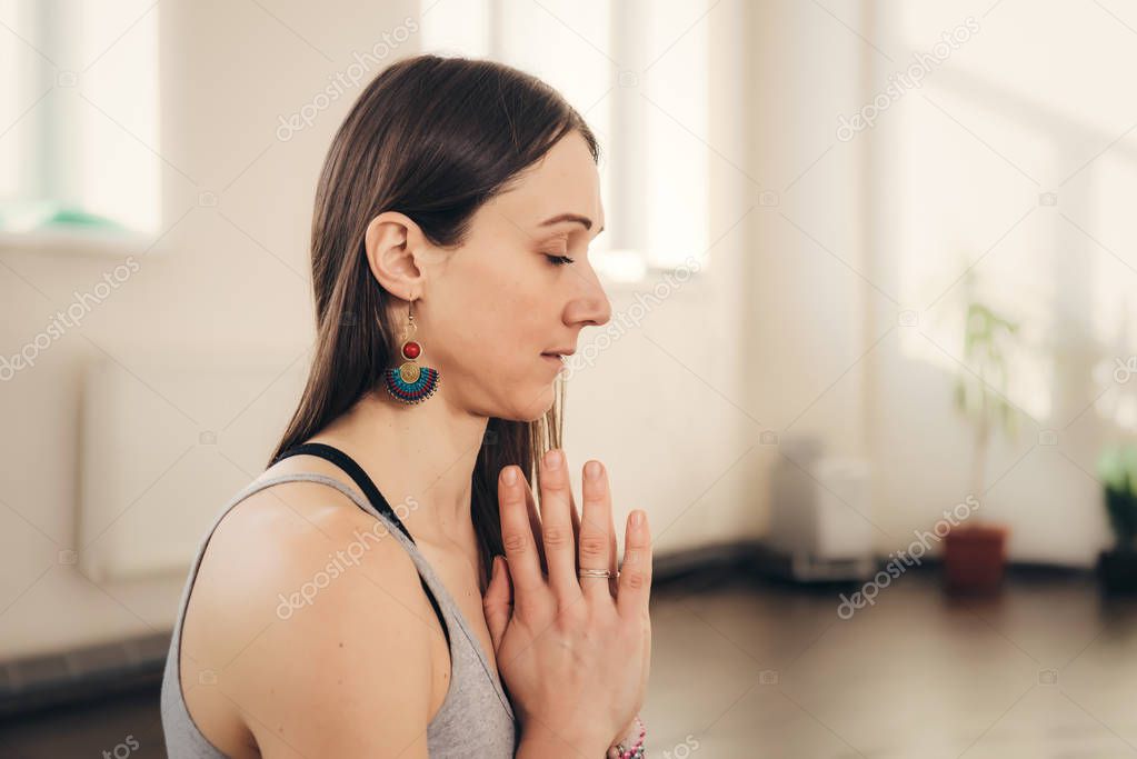 Portrait of beautiful young woman meditating and doing namaste hand gesture on a sunny morning at studio.