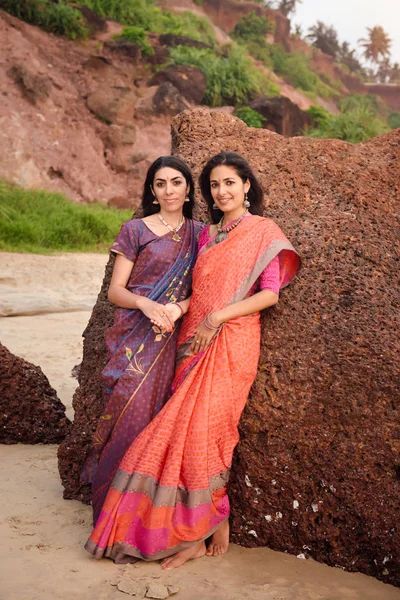 Fashion shoot of indian woman in traditional clothes. Friends girl in beautiful saree standing on the rock near the sea in saree at sunset