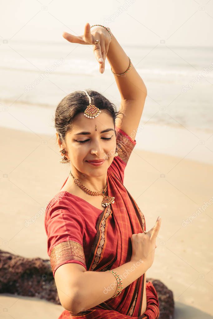 Indian classical dance Bharatanatyam performed by beautiful woman in traditional clothes at sunset