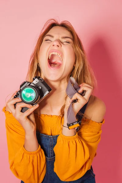 Blonde girl with retro style film camera on pink background