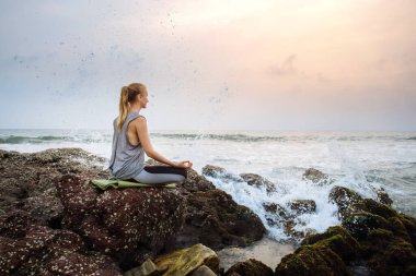 Sahilde yoga yapan genç bir kadın.
