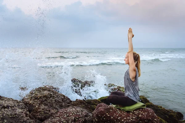 Mujer joven en la playa practica yoga en la orilla del mar — Foto de Stock