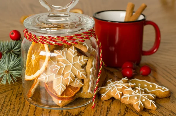 a mug decoration with two cinnamon sticks, gingerbread, glass jar with icing decorated cookies, christmas tree