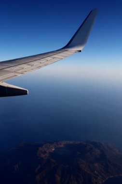Bir volkan adasının üzerinde uçan uçak kanadı - dikey