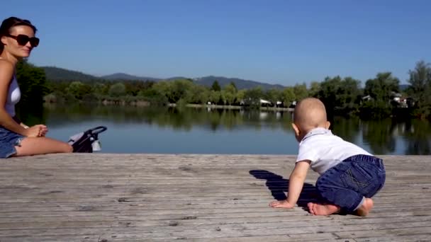 Un bébé rampant sur un quai en bois vers le lac. Maman le sauve. 4K — Video