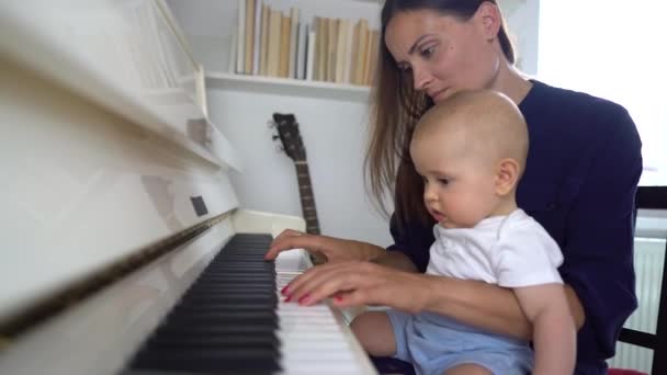 Uma linda mamãe tocando um piano branco com seu menino — Vídeo de Stock