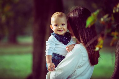 Ormanda gülümseyen bir bebeği tutan bir anne.