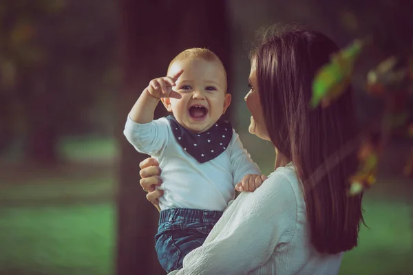 Une mère tenant un joli bébé souriant dans les bois — Photo