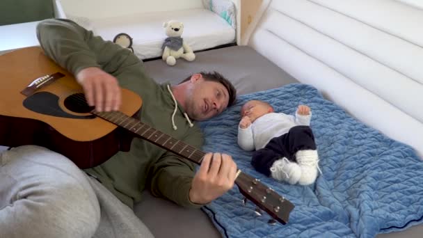 En kärleksfull far som spelar gitarr för sin son innan läggdags. 4K — Stockvideo
