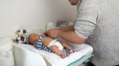 Tatlı bebeğini bebek bezi değiştirme masasında giydiren nazik bir baba. 4K