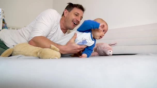 Un padre attraente che gioca con il suo bambino su un letto 4K — Video Stock