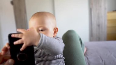 Sevimli bir erkek bebek cep telefonunu yatak başlığı 4K 'da ısırıyor.