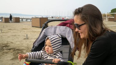 Annesiyle kumlu bir plajda bebek arabasında tatlı bir oğlan. Denizde yanındayız.