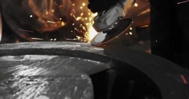Metal açı öğütücüsünde kıvılcımlar çıkıyor. Öğütücünün dönen diskinin etrafında bir sürü parıldayan kıvılcım uçuşuyor..