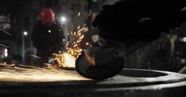 Metal açı öğütücüsünde kıvılcımlar çıkıyor. Öğütücünün dönen diskinin etrafında bir sürü parıldayan kıvılcım uçuşuyor..