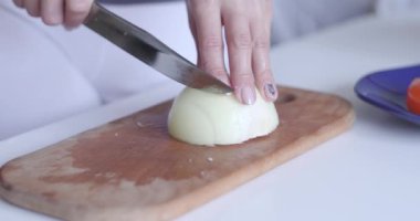 Kesme tahtasındaki soğan. Bıçaklı bir kadının elleri kesme tahtasındaki soğanı dilimliyor. Masadaki soğan..
