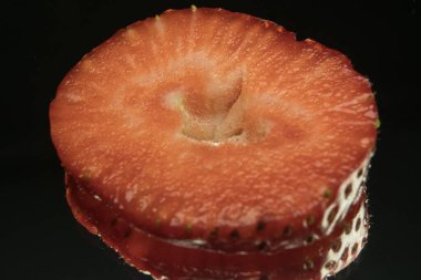 Çilek dilimleri, makro shot, siyah ayna arka planı. Çilekler vitamin bakımından zengindir.