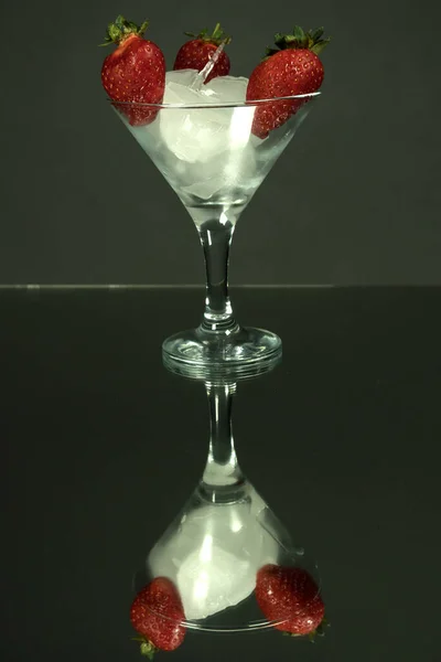 氷とイチゴの果実の部分と背の高いマティーニグラス 鏡暗い背景 — ストック写真