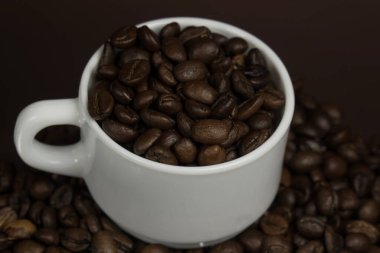 Koyu bir fonda kahve taneleri serpiştirilmiş beyaz kupa.