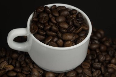 Koyu bir fonda kahve taneleri serpiştirilmiş beyaz kupa.