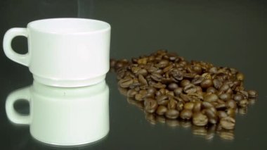 Beyaz fincandan duman, kahve çekirdekleri, gri-yeşil arka planda. Makro