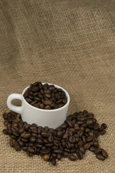 Freshly made coffee in a white cup surrounded by coffee beans on a wooden table. Fresh roasted coffee.