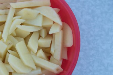 Kırmızı plastik bir tabakta dilimlenmiş çiğ patates. Açık hava barbeküsü