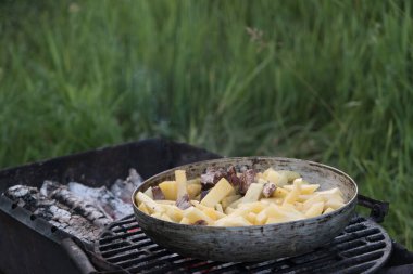 Ceket patatesleri, kabak ve sosisler açık ateşte büyük bir kızartma tavasında pişirilir. Doğada barbekü.