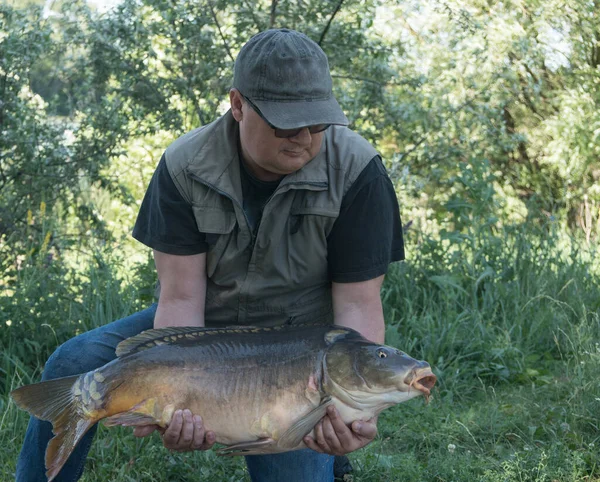 Carp fishing. Fisherman with fish trophy in hands at lake. Big carp.