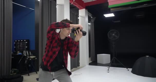 Joven guapo fotógrafo profesional masculino tomando fotos de una modelo en un estudio. Él está satisfecho con las imágenes capturadas . — Vídeos de Stock