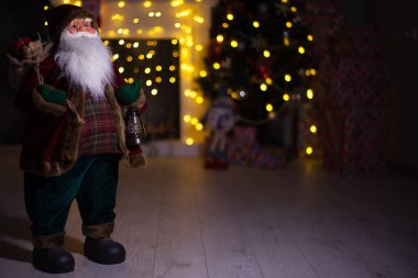 Noel Baba hediye dolu büyük bir çanta taşıyor, Noel ağacının yanında.