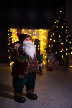 Noel Baba hediye dolu büyük bir çanta taşıyor, Noel ağacının yanında.